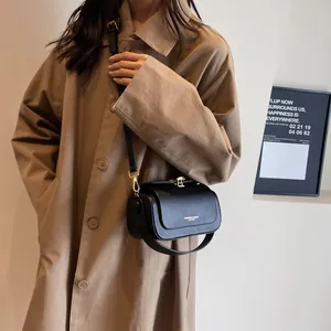 Classic black leather square crossbody bag with metallic clasp worn with a beige trench coat