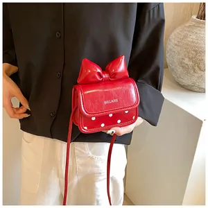 Détail d'un petit sac bandoulière rouge avec un grand nœud et motif à pois blancs