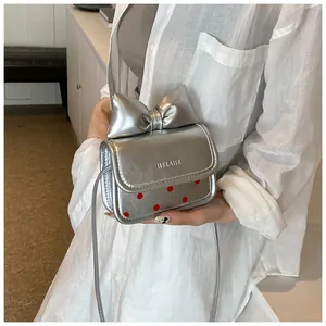 Détail du sac bandoulière argenté avec nœud et pois rouges porté sur chemise blanche