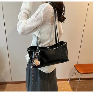 Detail of glossy black faux leather shoulder bag with decorative woven pendant and charms