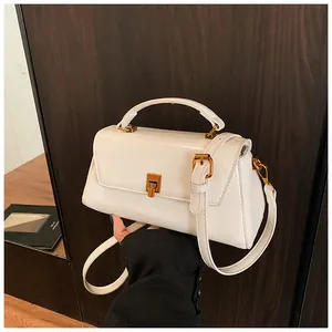 Detail of white square handbag showing golden metal twist lock and leather texture