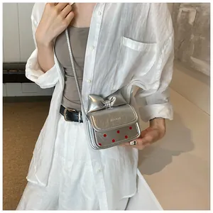 Détail du mini sac bandoulière argenté avec nœud et pois rouges sur chemise blanche