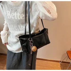 Detail of glossy black shoulder bag with brown textured pendant and dual straps