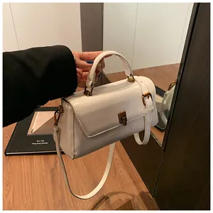 Detail of white mini square handbag with gold metal lock being held by hand
