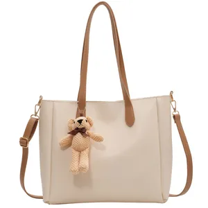 Minimalist cream tote bag with brown straps and cute knitted bear charm on white background