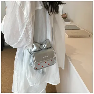 Détail du sac bandoulière argenté avec grand nœud et motifs à pois rouges
