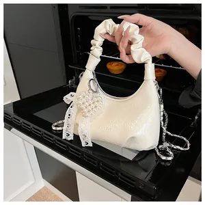 Detail of creamy white ruched cloud bag with pearl heart charm and lace bow decor