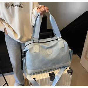 Détail du sac de voyage bleu clair texturé posé sur la poignée d'une valise blanche