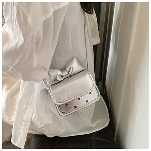 Détail d'un mini sac bandoulière argenté avec grand nœud et motif à pois rouges