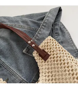 Detailed view of woven straw tote bag with brown leather strap and silver metal rivets