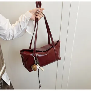 Close-up of glossy wine red leather tote bag with a baseball glove charm on the strap