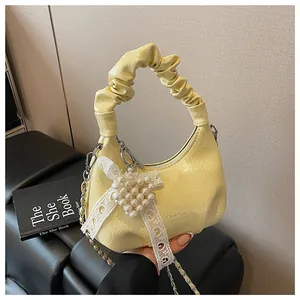 Detail of light yellow ruched cloud bag featuring pearl heart charm and metal chain
