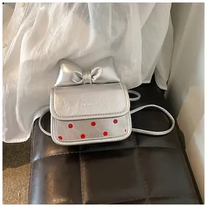 Détail du mini sac bandoulière argenté avec nœud et pois rouges sur un tabouret en cuir