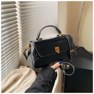 Detail of glossy black handbag with golden metal square buckle and leather texture