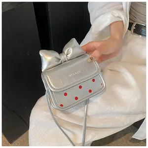 Détail du mini sac argenté avec un grand nœud métallique et motif à pois rouges sur le rabat