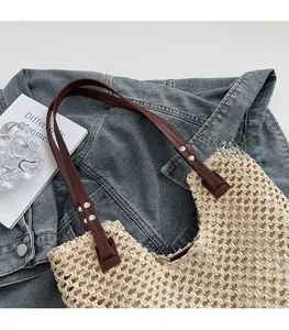 Close-up of woven straw tote bag with brown leather straps and metallic rivets on denim