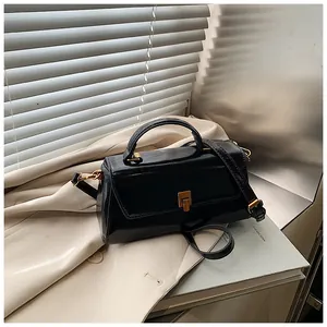 Detail of black glossy handbag with golden metal turn-lock and adjustable shoulder strap