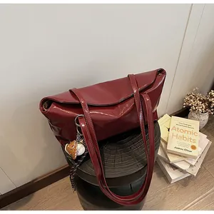 Macro view of burgundy patent leather bag featuring a baseball glove charm and flap closure