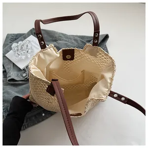 Detail view of woven straw tote bag featuring magnetic closure and brown leather straps