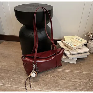 Detail of burgundy waxed leather shoulder bag with creative baseball glove charm decoration