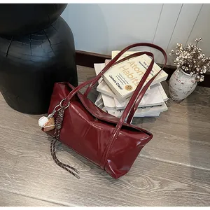 Detail of dark red glossy leather shoulder bag with a creative baseball charm on a strap