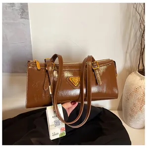 Detail einer braunen glänzenden Schultertasche mit goldenem Dreieckslogo und Reißverschluss