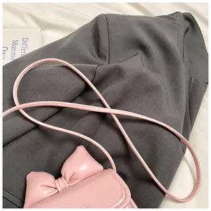 Gros plan d'un mini sac bandoulière rose en cuir avec un nœud sur un blazer gris