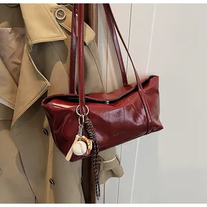 Detail of burgundy wax leather shoulder bag with baseball charm on a beige coat