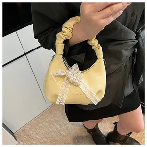 Detail view of yellow pleated bag featuring pearl cluster and lace bow decoration