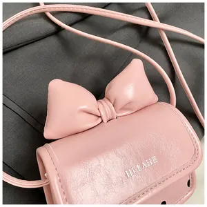 Gros plan du mini sac rose à bandoulière avec grand nœud et logo HELAHE blanc