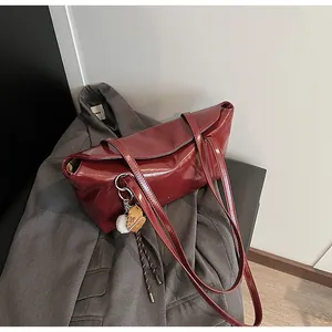 Detail of burgundy glossy oil-wax leather handbag with a baseball glove charm accessory
