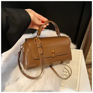 Close-up of brown glossy leather square handbag with top handle and bronze hardware details