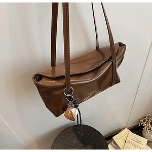 Detail of a dark brown oil-wax leather shoulder bag with a baseball glove charm accessory