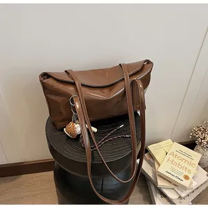 Brown waxed leather tote bag detail with sports charms on a minimalist black stool