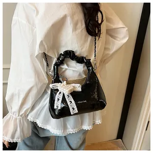 Detail of black patent leather bag with ruched handle and pearl lace heart pendant