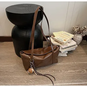 Detail of a brown oil-wax leather shoulder bag with a unique charm on wood decor