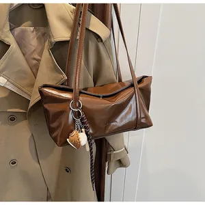Detail of dark brown oil-wax leather shoulder bag with logo and baseball pendant accessory