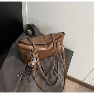Close-up of brown polished leather bag with dual straps and a cute bear charm accessory