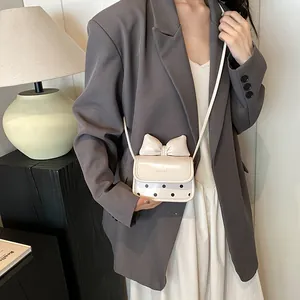 Mini sac bandoulière beige chic avec nœud et pois porté par un mannequin en costume