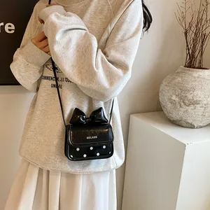 Mini sac bandoulière noir avec nœud et pois porté par un mannequin en décor minimaliste