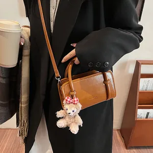 Brown glossy leather handbag with teddy bear charm and round handle for women