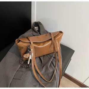 Detail of a brown oil wax leather shoulder bag with a baseball-themed keychain on a blazer