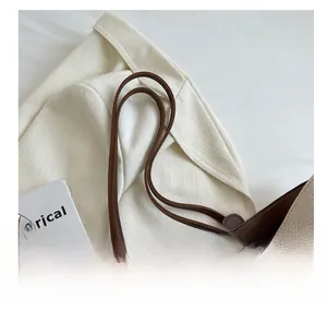 Detail of beige canvas tote with brown leather handles and dark red lining