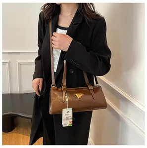 Nahaufnahme braune glänzende Ledertasche mit goldenem Dreieckslogo auf schwarzem Blazer