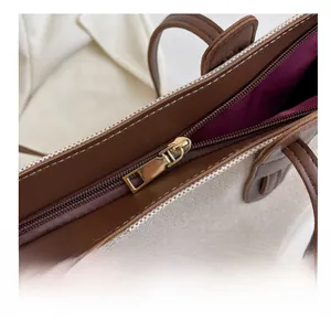 Detail of a smooth gold metal zipper and brown leather trim on a canvas tote bag