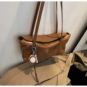 Detailed close-up of brown oil-wax leather shoulder bag with a mini baseball keychain