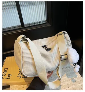 Detail of off-white corduroy dumpling bag with plush charm and wide canvas shoulder strap