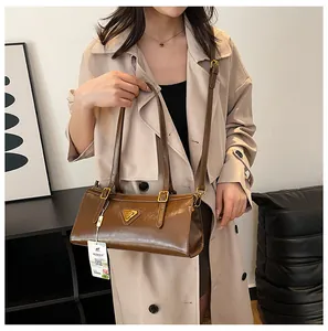 Nahaufnahme der braunen glänzenden Ledertasche mit goldenem Dreieckslogo und Trageriemen