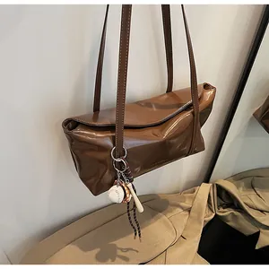 Detail of dark brown glossy leather tote bag with flap closure and baseball bag charm