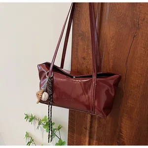 Detail of burgundy glossy leather shoulder bag with chic baseball glove pendant charm